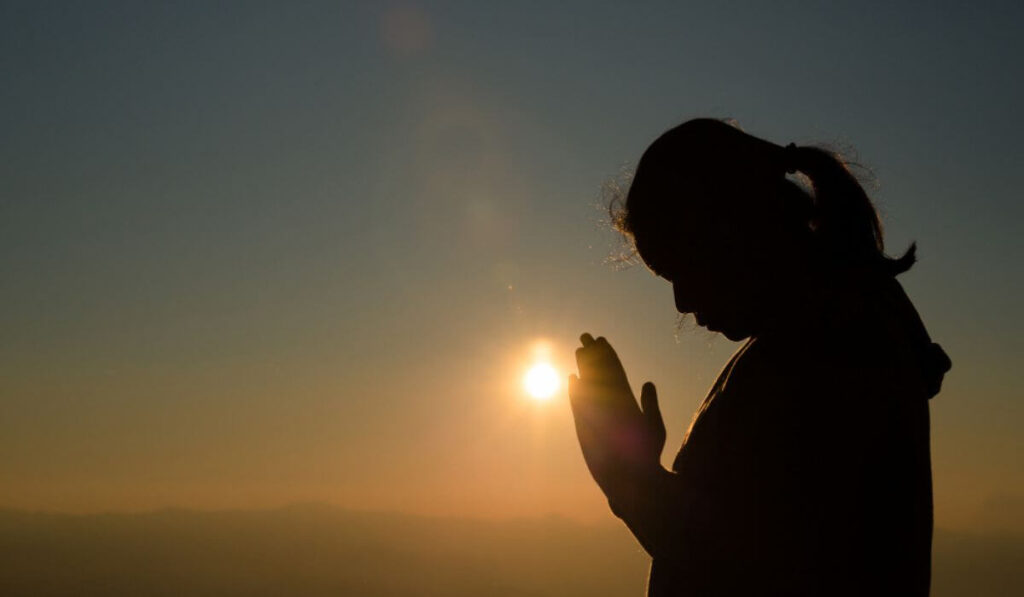 silhouette of woman praying to the sun